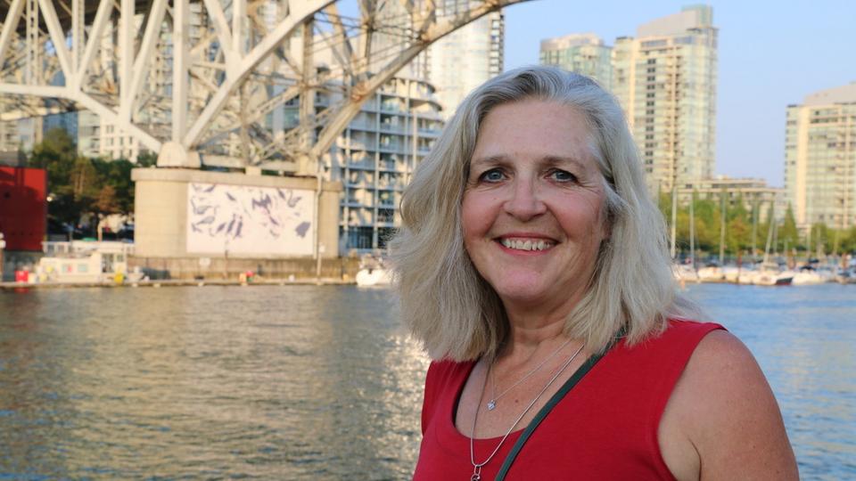 Portrait photo of woman in red dress standing near water and a bridge